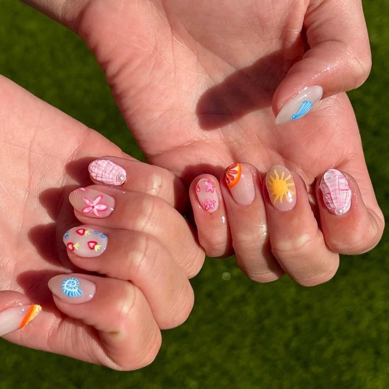Oval nails with mismatched seashells suns and floral designs