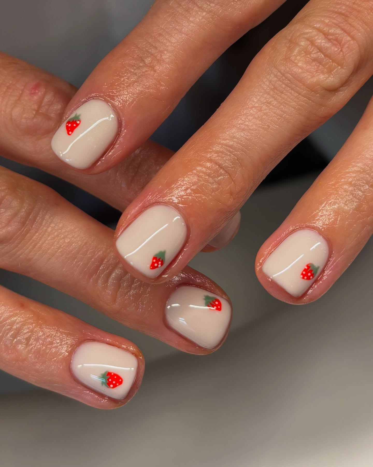 Milky white nails with tiny painted red strawberry corner accents