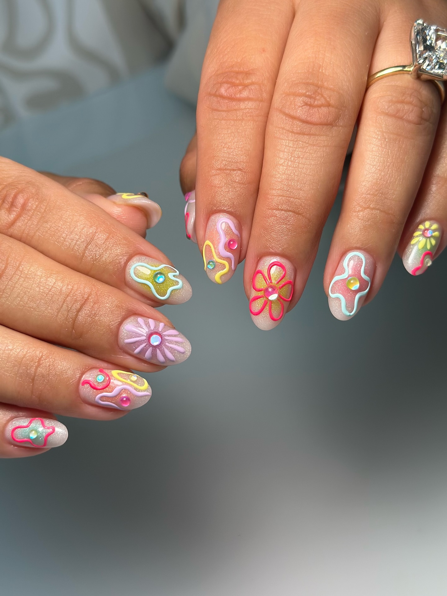 Sheer almond nails with neon swirl shapes and rhinestone daisies