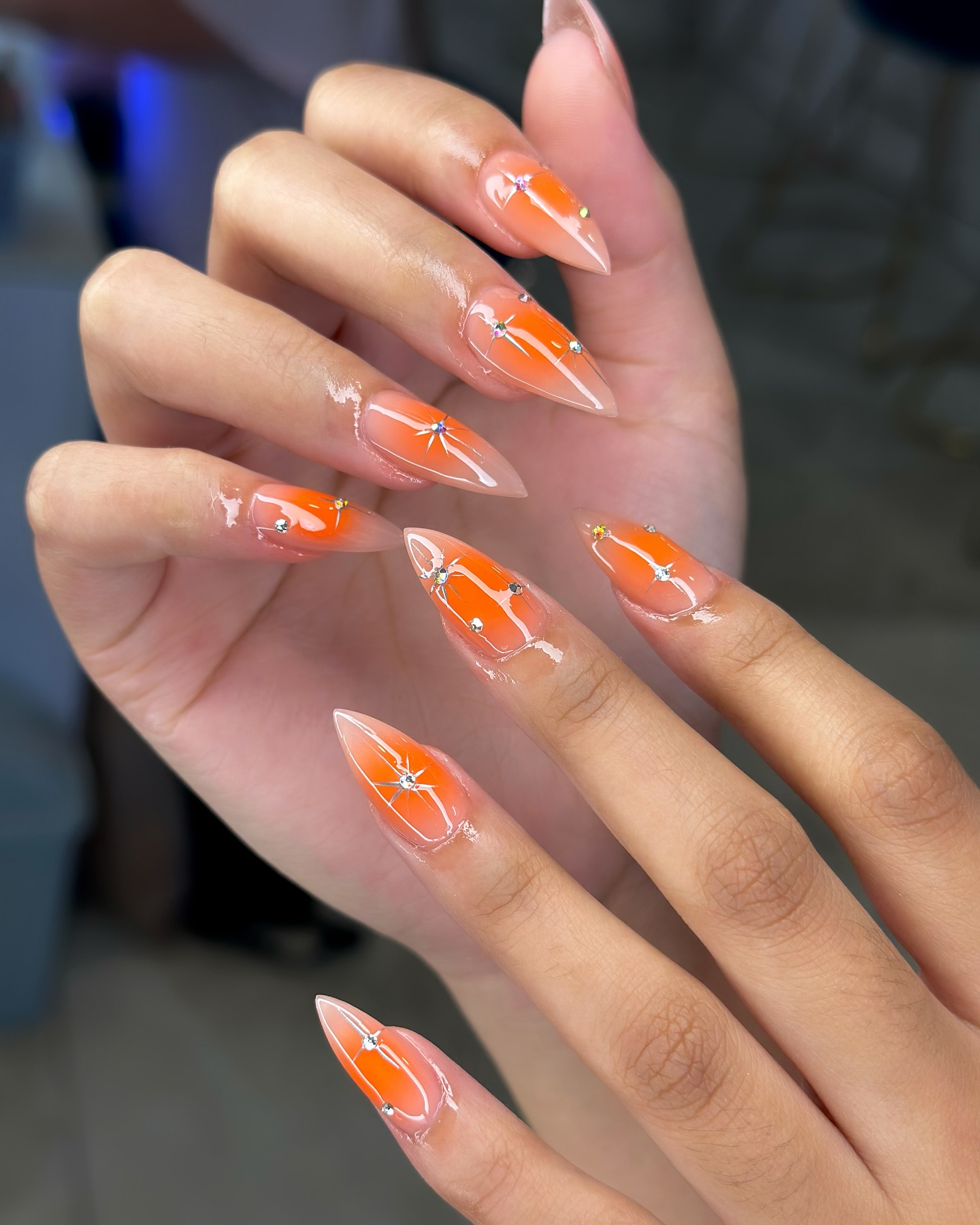 Sheer orange jelly almond nails with iridescent gems