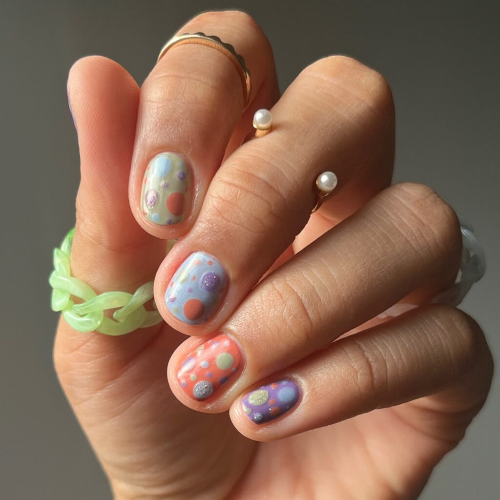 short nails in pastel yellow, blue, peach, and purple with multicolour confetti dots
