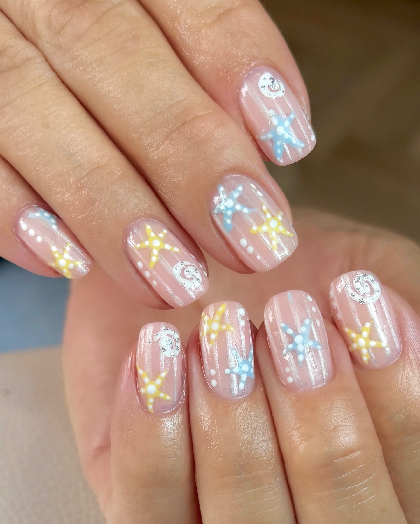 Pearlescent pink nails with yellow and blue starfish and silver shell accents