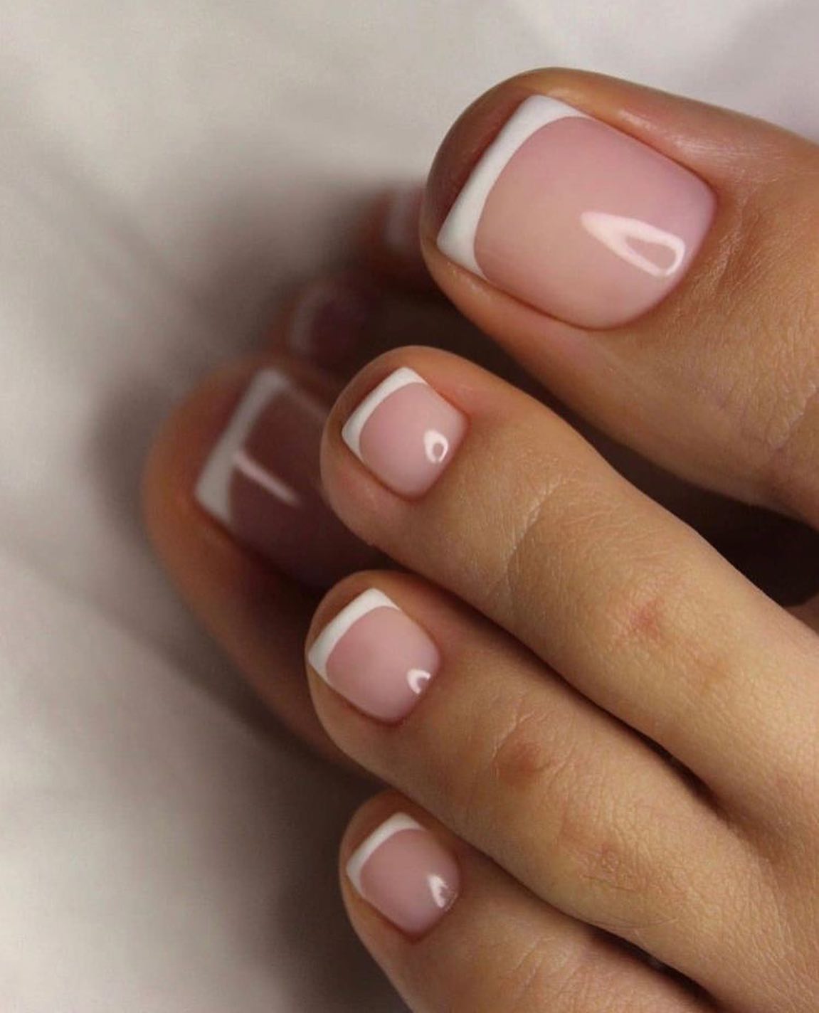 Clean classic pink and white French tip toe nails close-up on soft white background