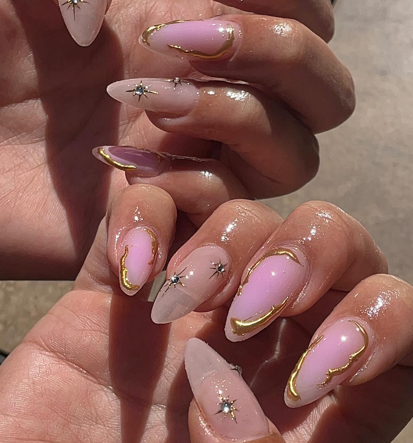 Blush pink almond nails with gold swirls and star gems