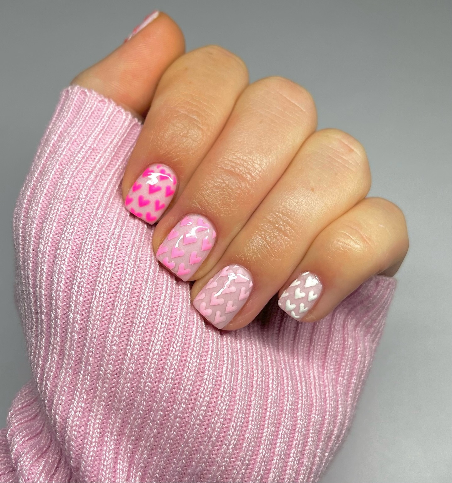 Short square nails covered in hearts progressing from hot pink to white across the hand