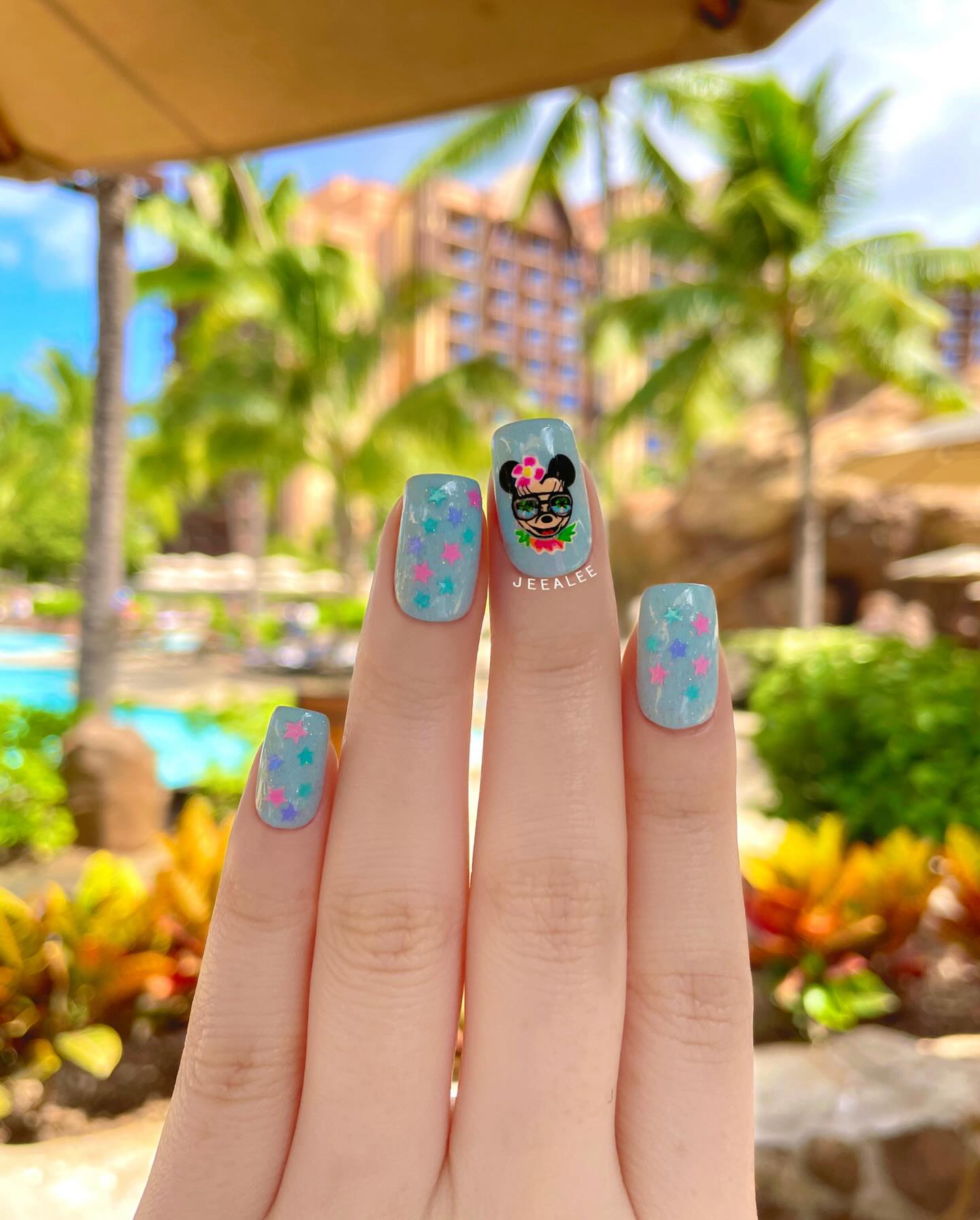 Sage blue nails with pastel star confetti at a resort pool