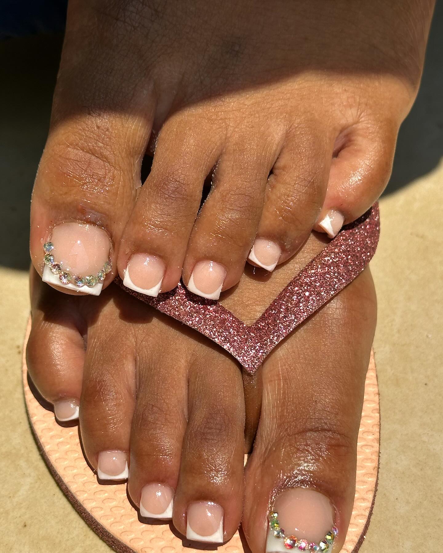 Classic white square French tip toe nails with a row of sparkling AB rhinestones on the big toe worn in pink glitter flip flops