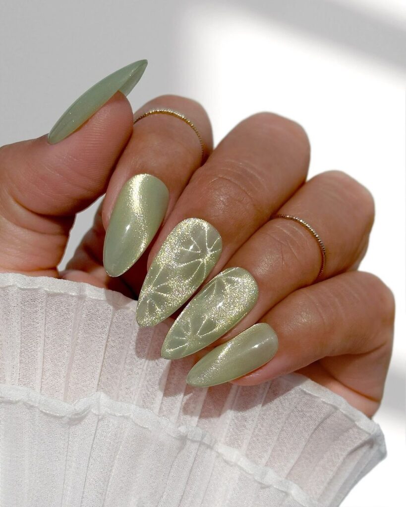 Long stiletto sage green chrome nails with gold shimmer and geometric glitter detail
