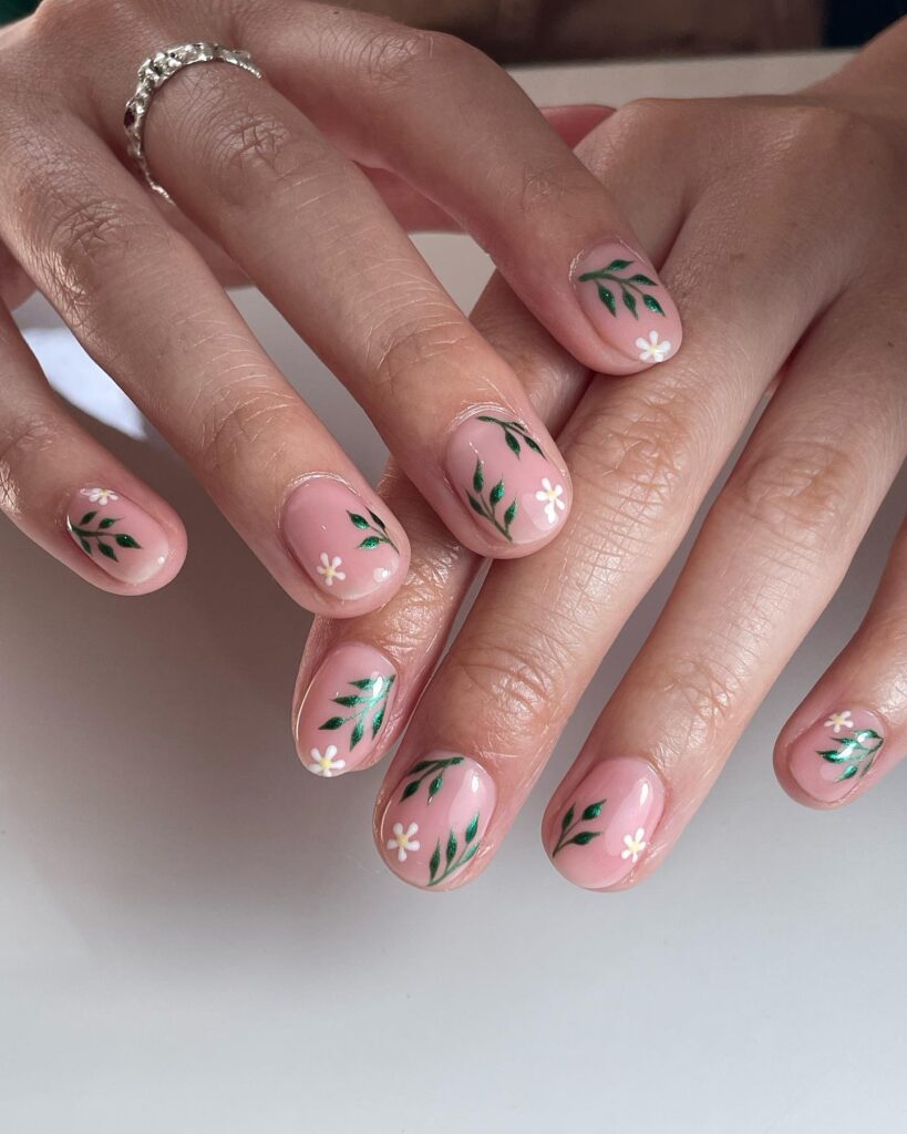 Short sheer pink nails with painted emerald green leaf sprigs and tiny white daisy details
