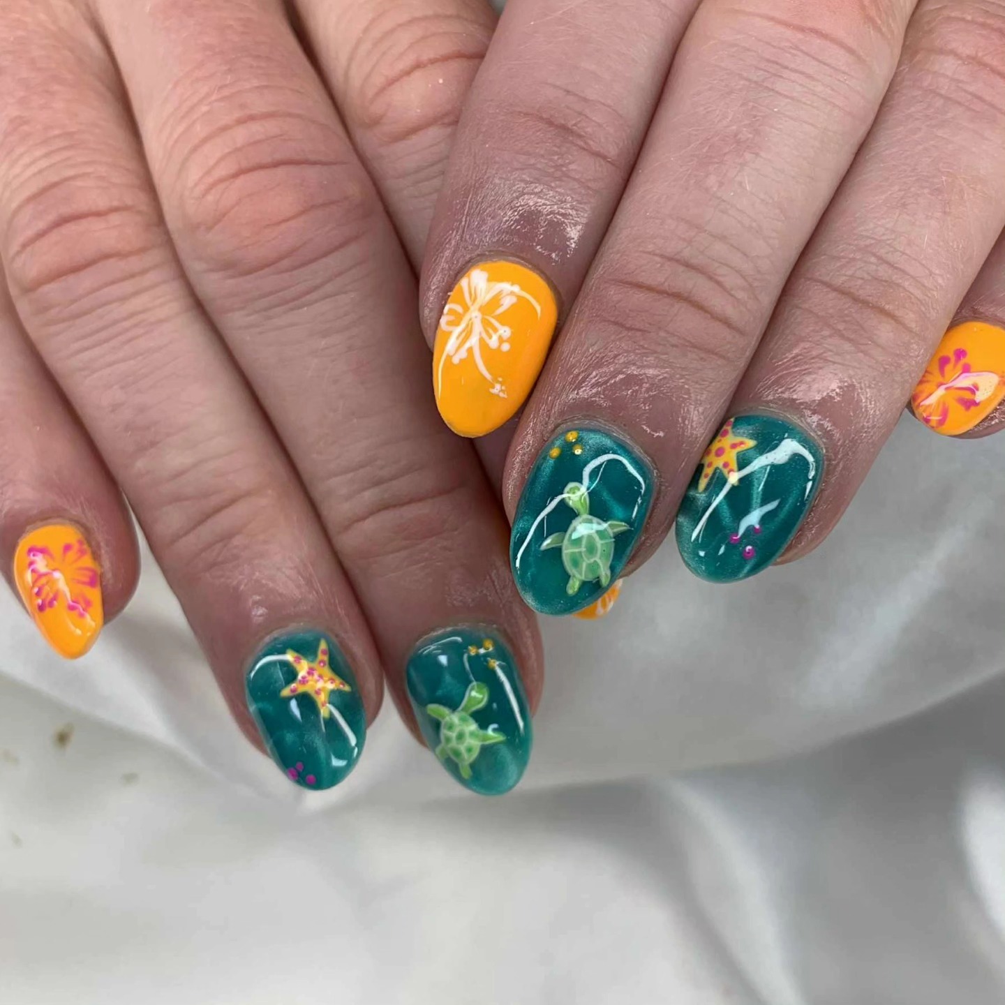 Teal ocean nails with painted sea turtles and starfish alongside vivid orange nails