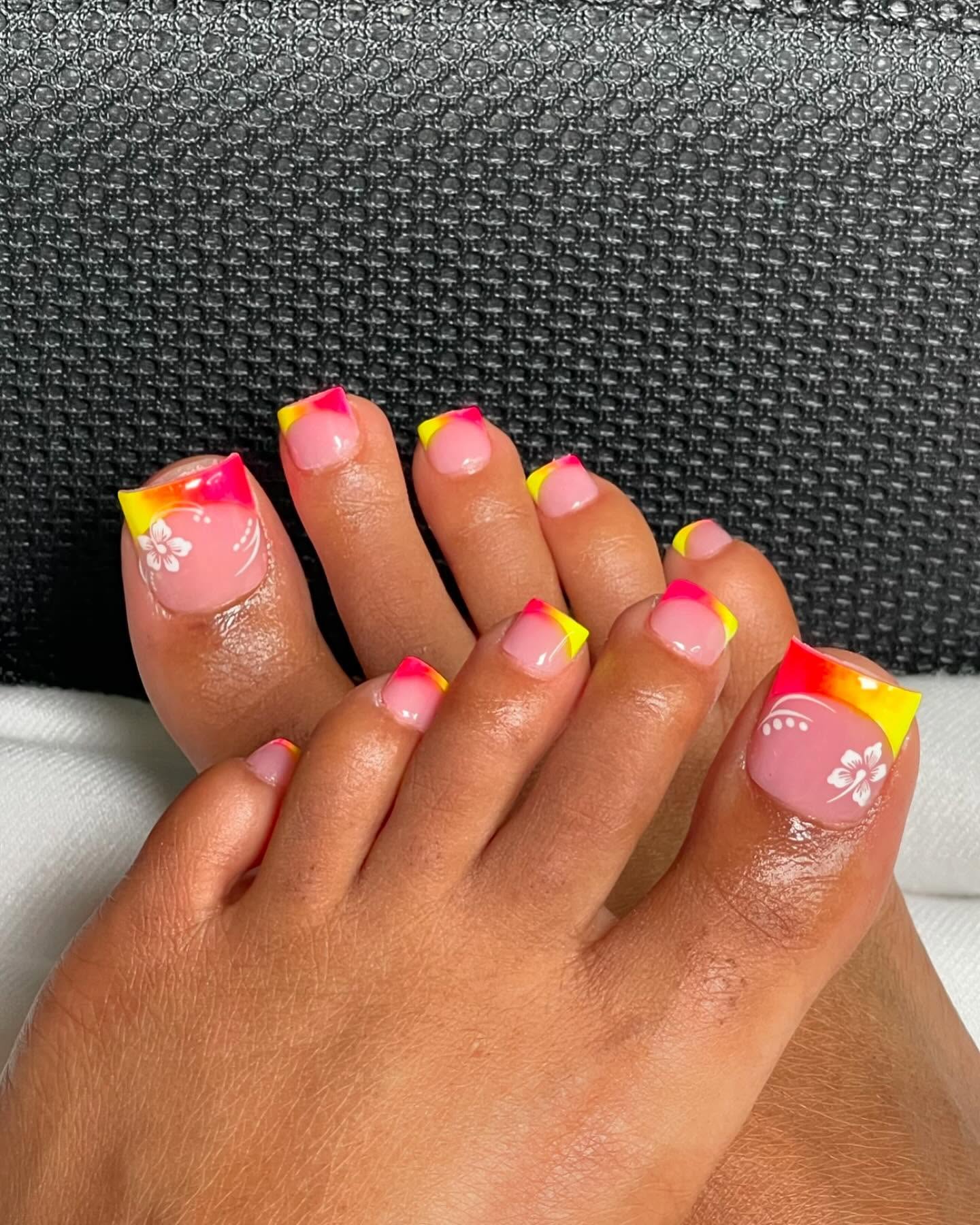 Tropical sunset French toe nails with pink and yellow gradient tips and white hibiscus flower art on big toe