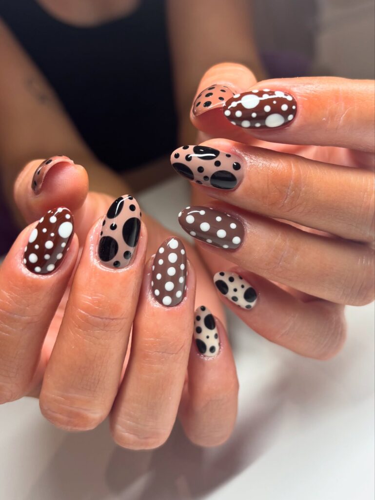 Almond nails in mocha brown and taupe with large overlapping black and white polka dots in an abstract graphic pattern