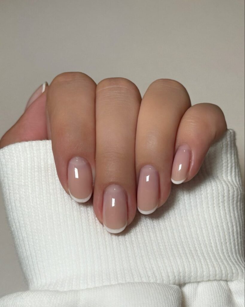 Short round nails with a very fine white French tip line on a sheer nude-pink base