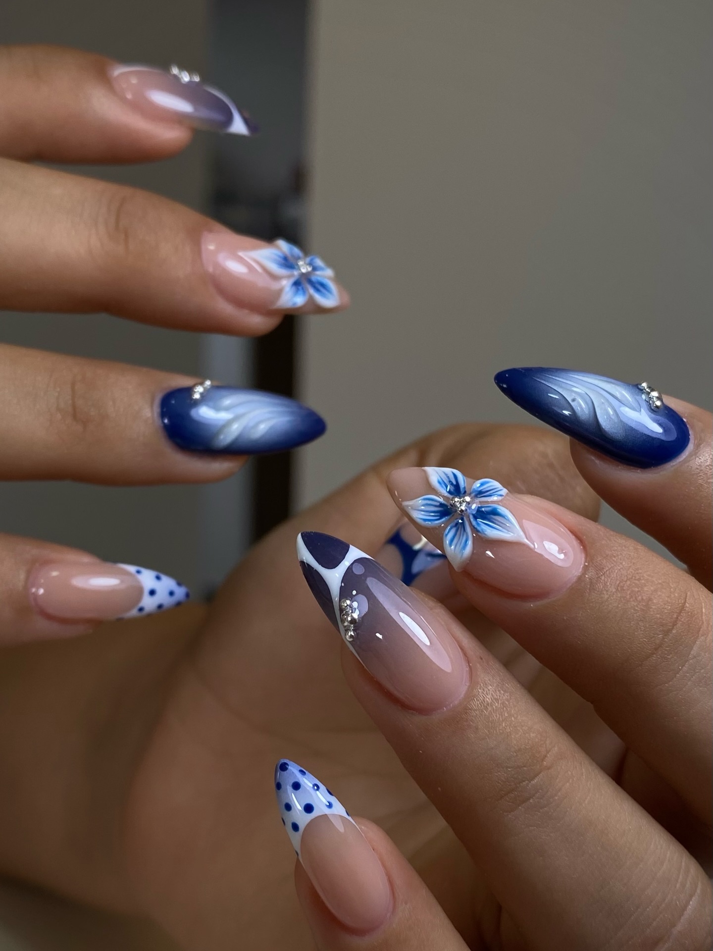 Almond nails with cobalt blue tips, 3D blue flowers, white swirls, and crystal rhinestones