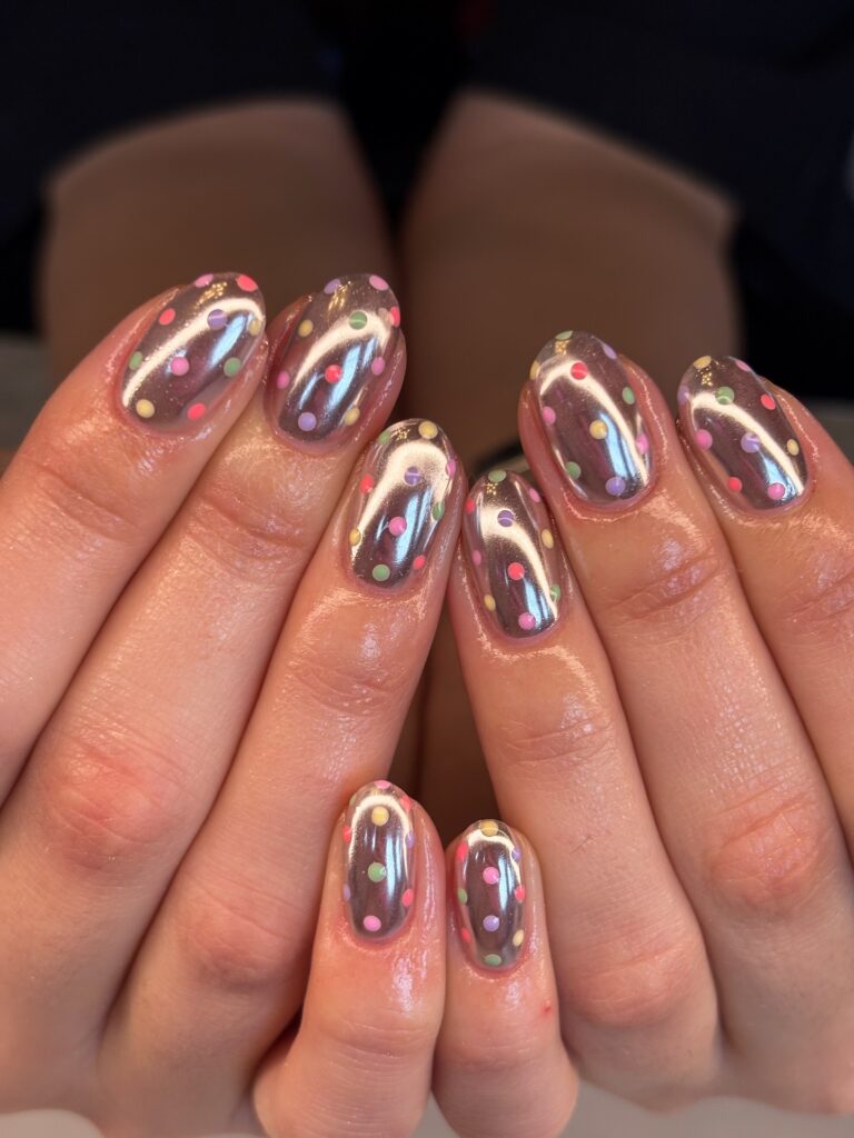 Short oval nails in rich dark chocolate brown scattered with multicolour confetti polka dots in pink, mint, peach, and yellow