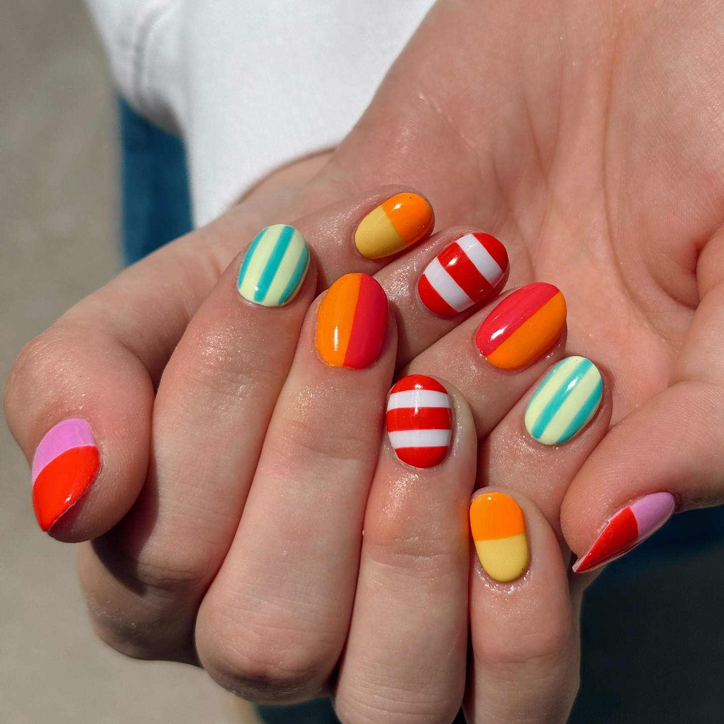 Short round nails in mismatched bold orange, red, and teal stripes
