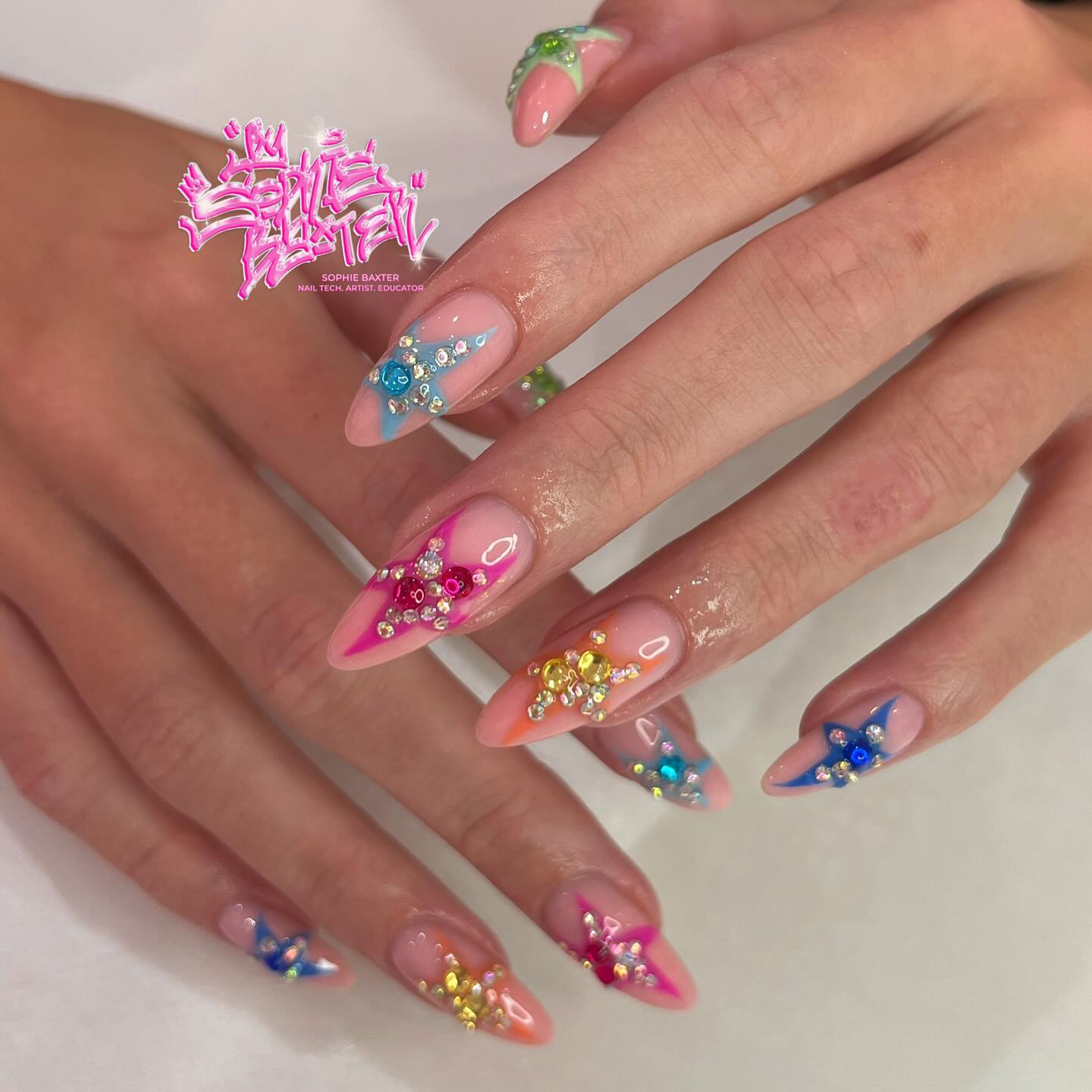 Pink almond nails decorated with bold multicolour rhinestone star and floral cluster designs