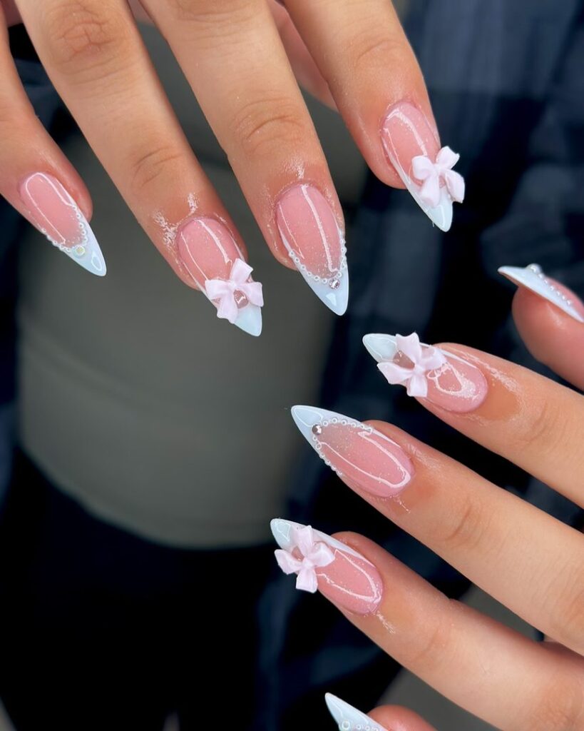 Long stiletto nails with ice blue-white French tips, delicate silver chain detail, and 3D pink bow charms at the tip