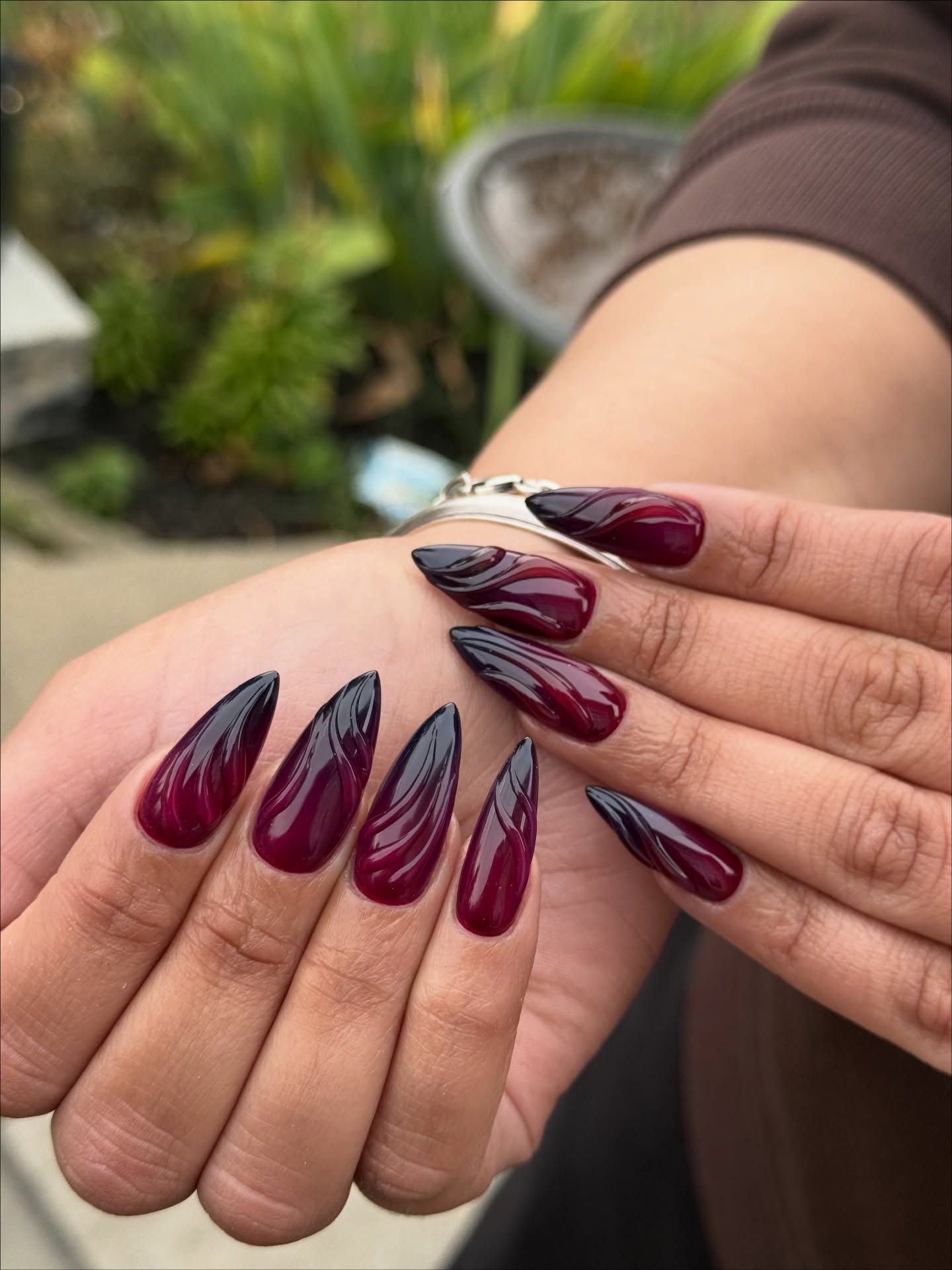 Long stiletto nails in deep burgundy red with bold black painted brushstroke swirl accents