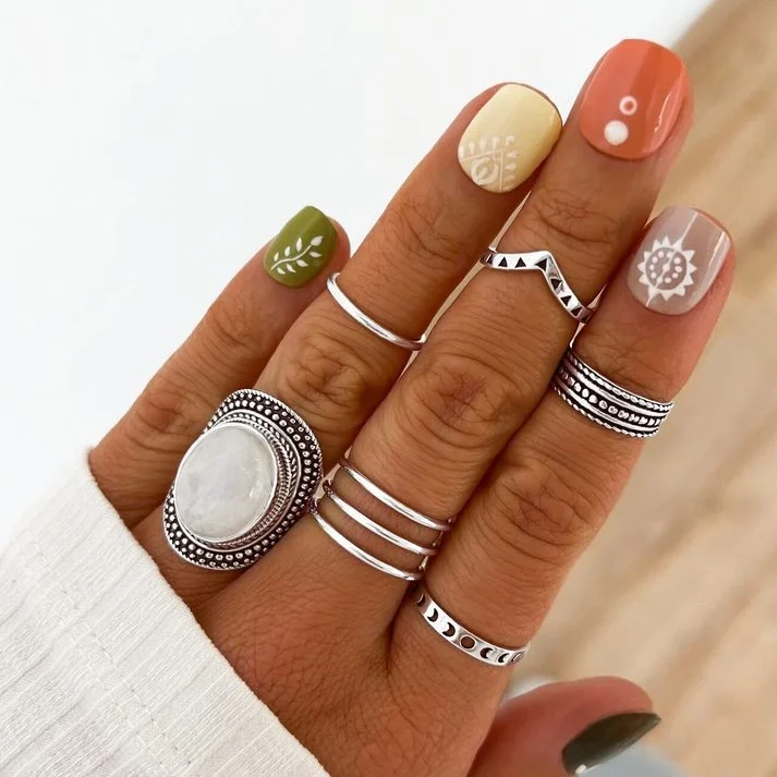 Short square nails in terracotta, olive green, mustard yellow and blush, each featuring hand-painted boho symbols