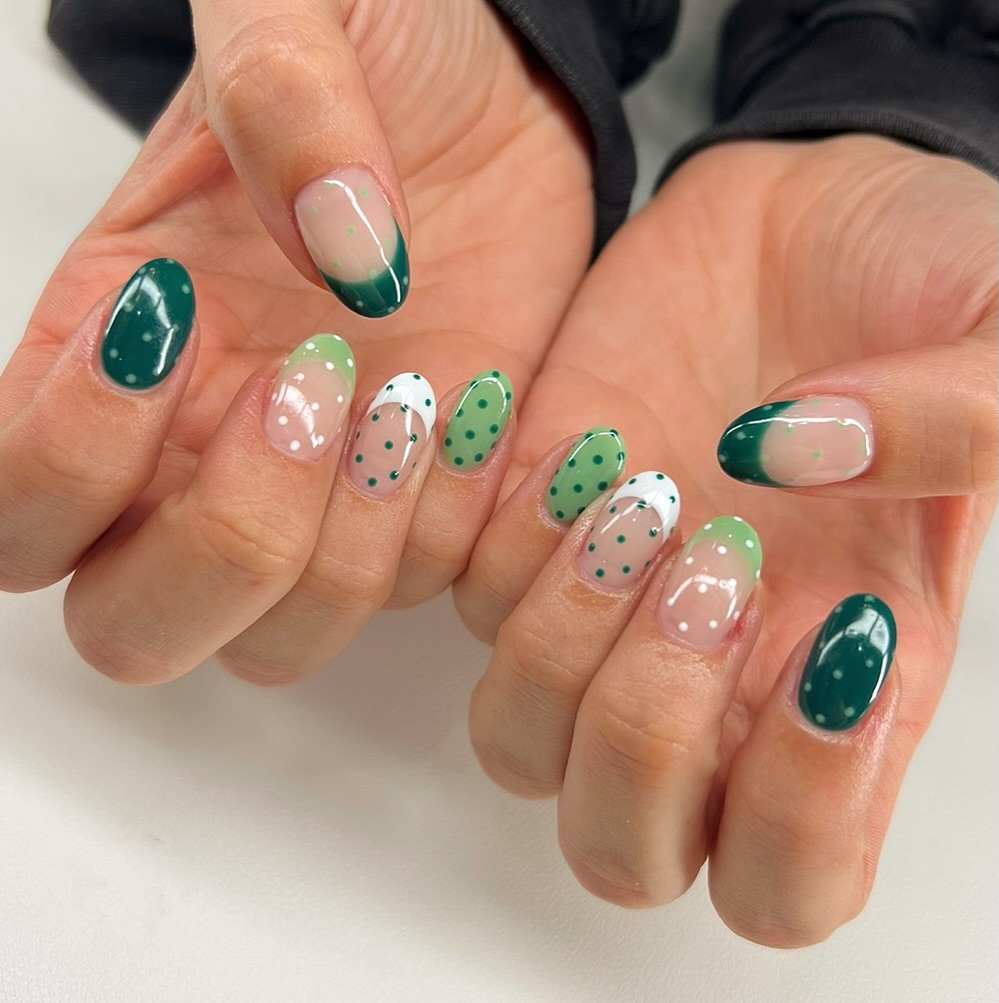 Mixed green nails combining deep forest green tips, white base with green polka dots, and sheer nails with dotted accent details