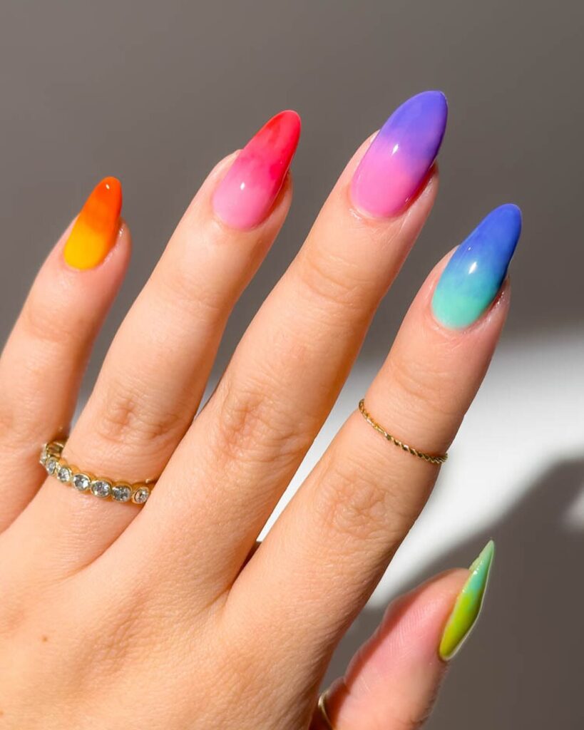 Long almond nails with each finger wearing a different vibrant rainbow ombre from orange to red to pink to purple to blue to green