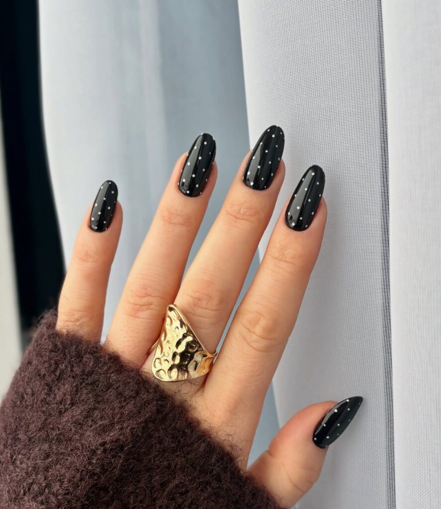 Glossy jet-black almond nails with evenly scattered tiny pearl-white polka dots
