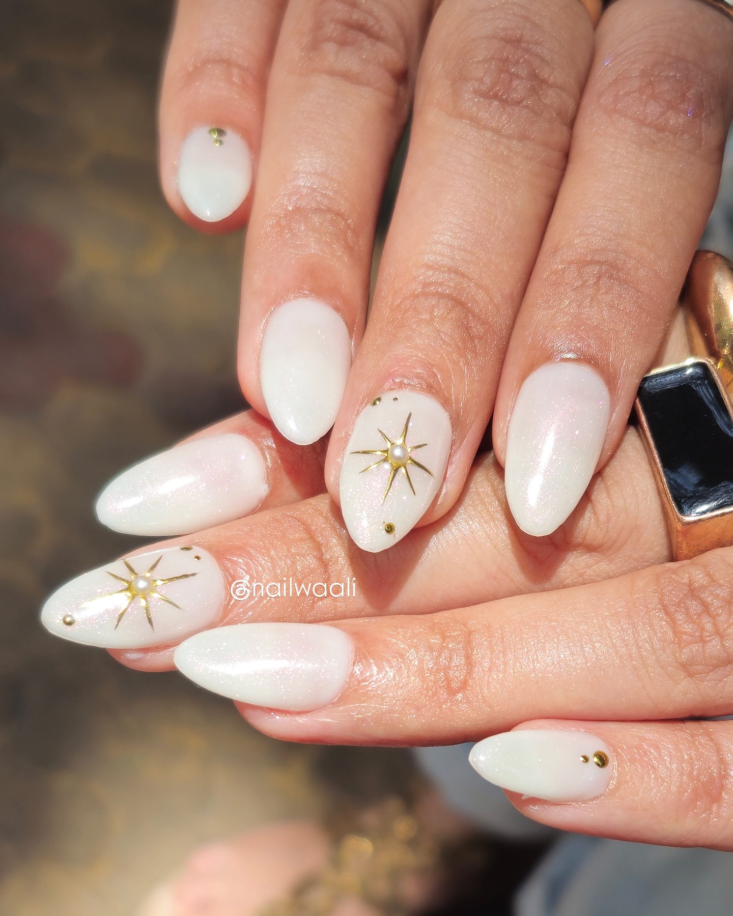 Long almond nails in creamy ivory white with pearlescent shimmer, gold north star motif, and pearl centre charm