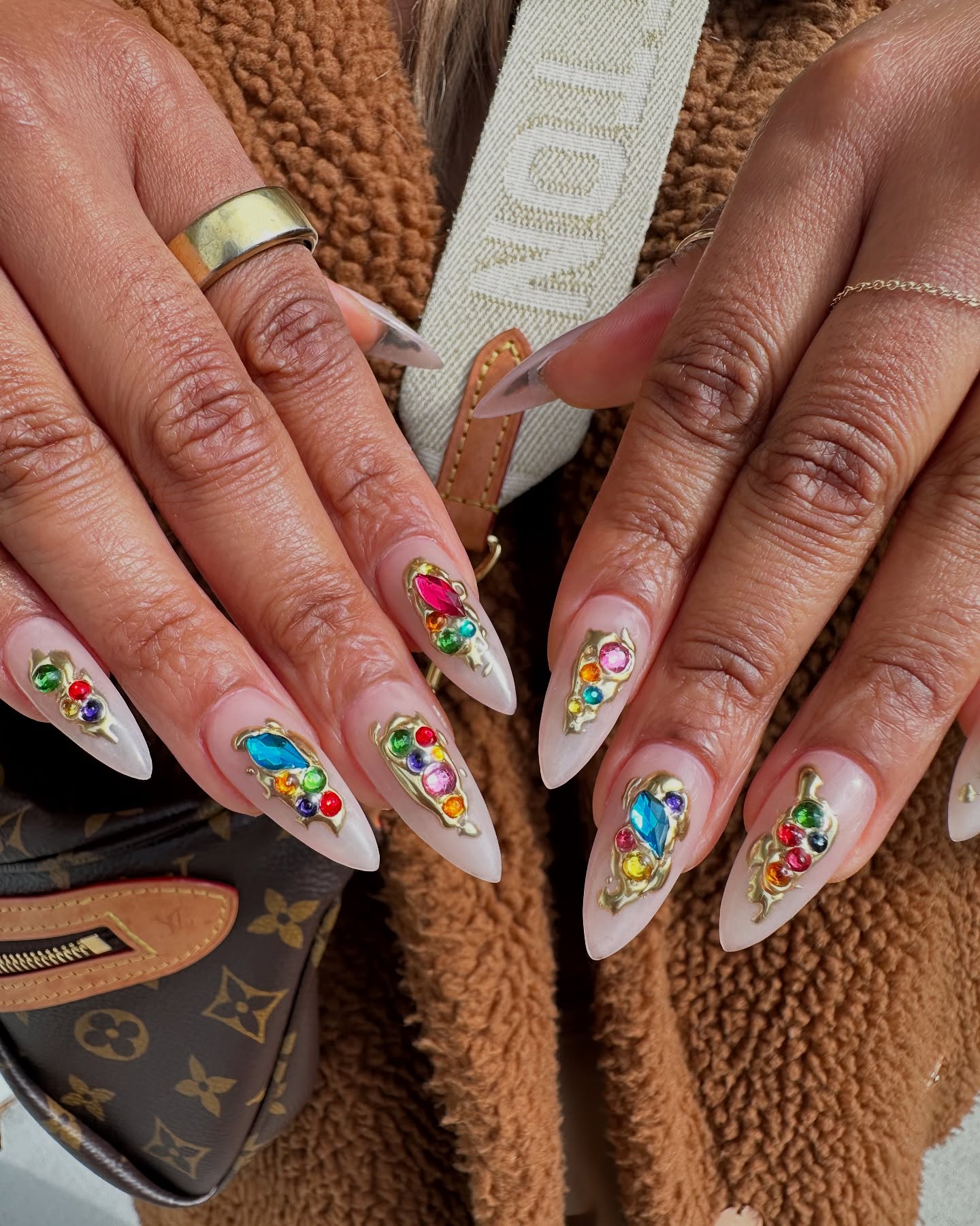 Cream stiletto nails adorned with large multicoloured gemstone clusters set in gold