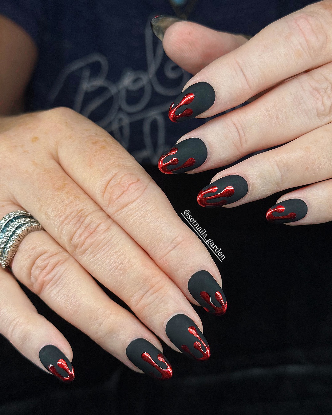 Long almond matte black nails with sinuous red flame drip accents along the sides