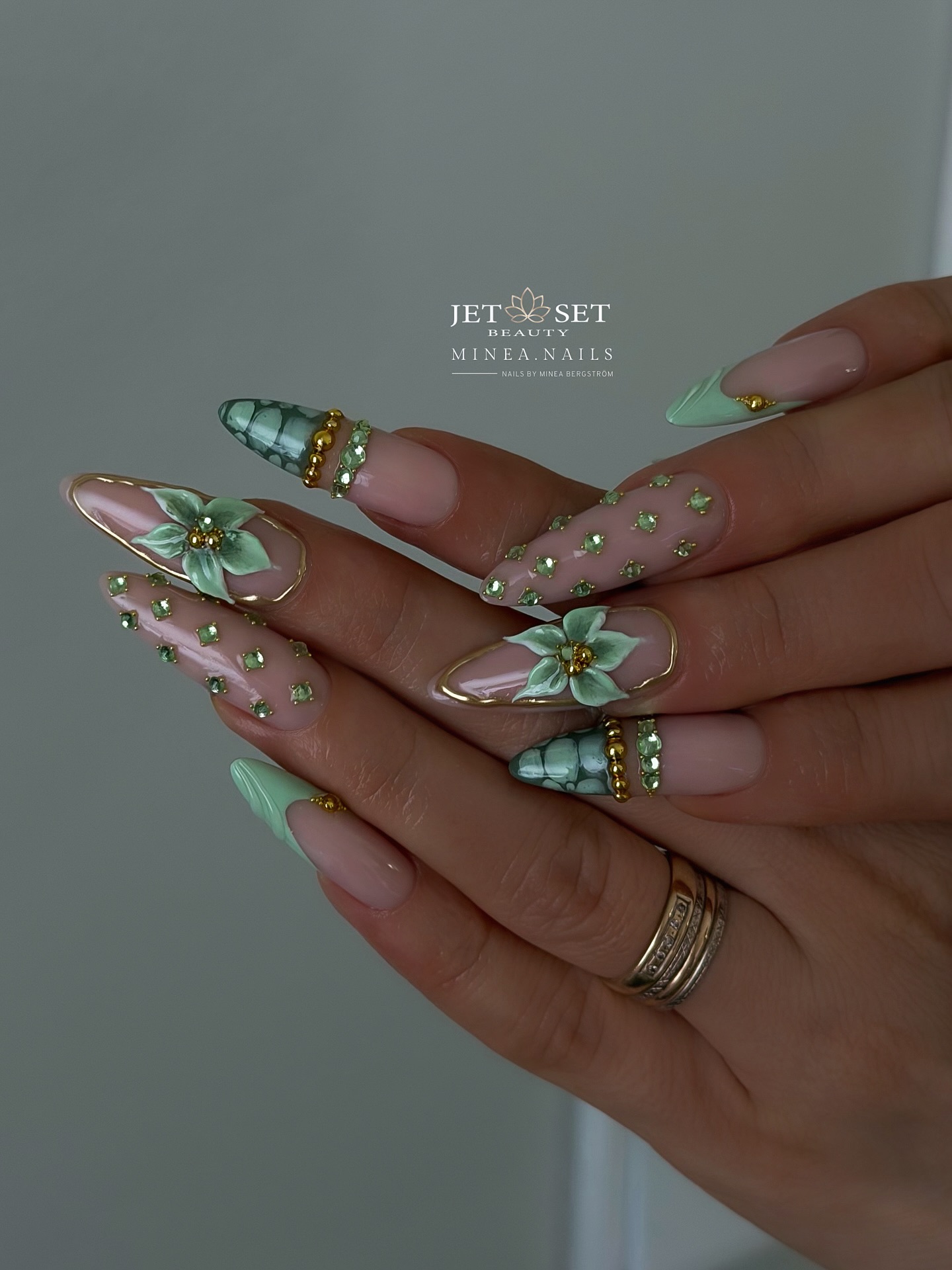 Long stiletto nails with mint green tips, 3D sculptural flowers, and scattered gold rhinestone studs