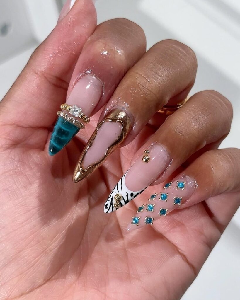 Long stiletto press-on nails with teal chrome tip, gold liquid metal tip, white-and-black zebra French tip, and teal rhinestone scatter