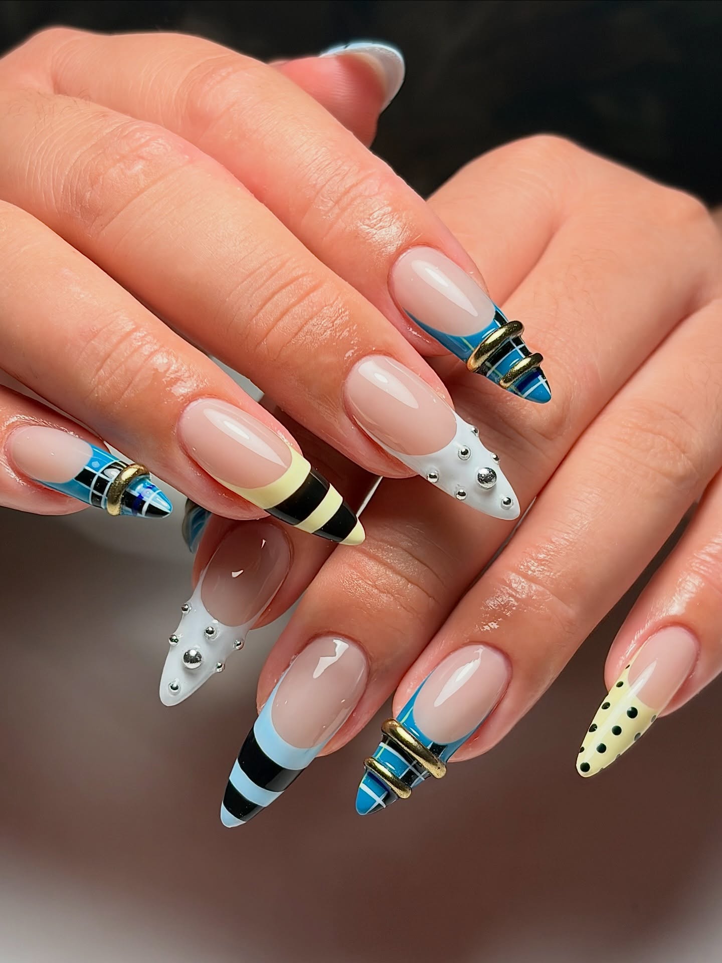 Stiletto French tips with blue, gold, and black stripes and pearls