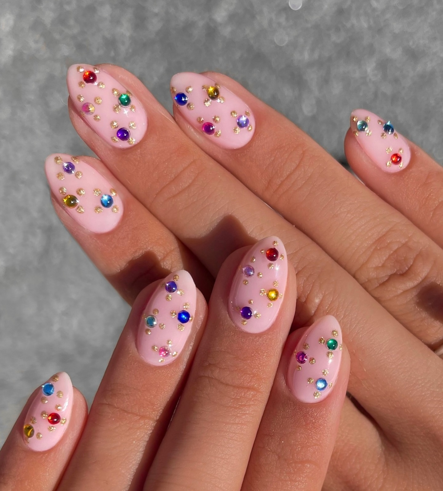 Soft pink almond nails covered in multicolour rhinestone confetti and gold studs
