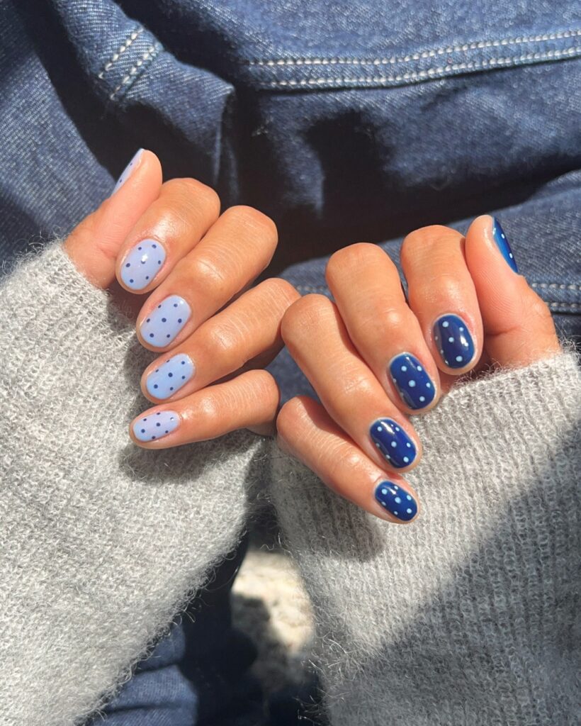 Short oval nails alternating between deep navy with white polka dots and sheer lavender blue with blue polka dots