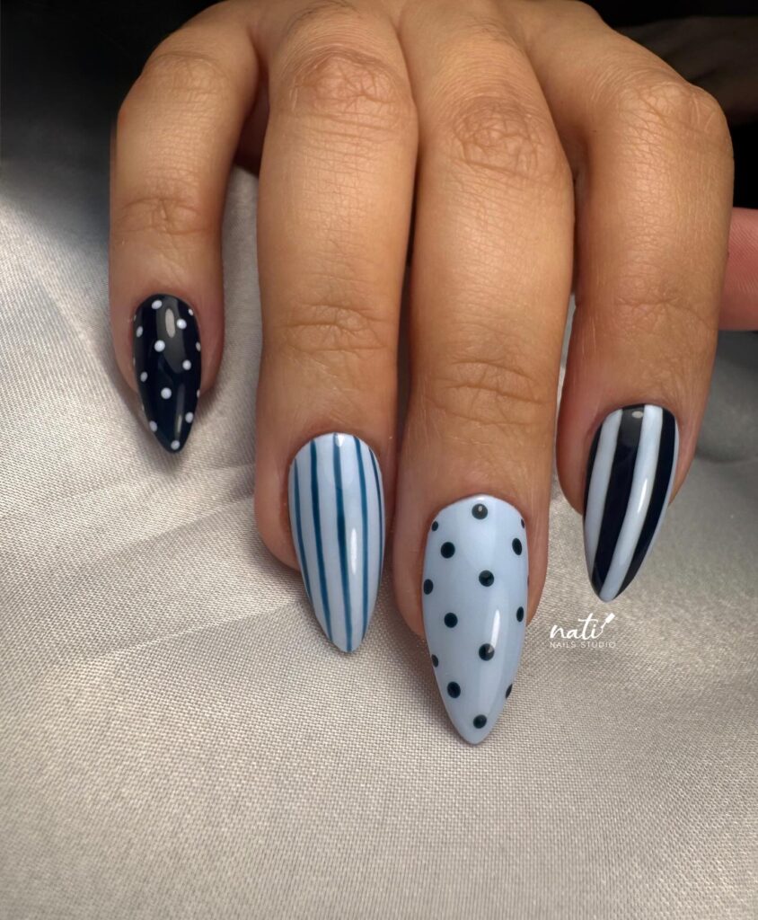 Stiletto nails mixing solid navy, pale ice blue with black polka dots, and graphic vertical stripe details