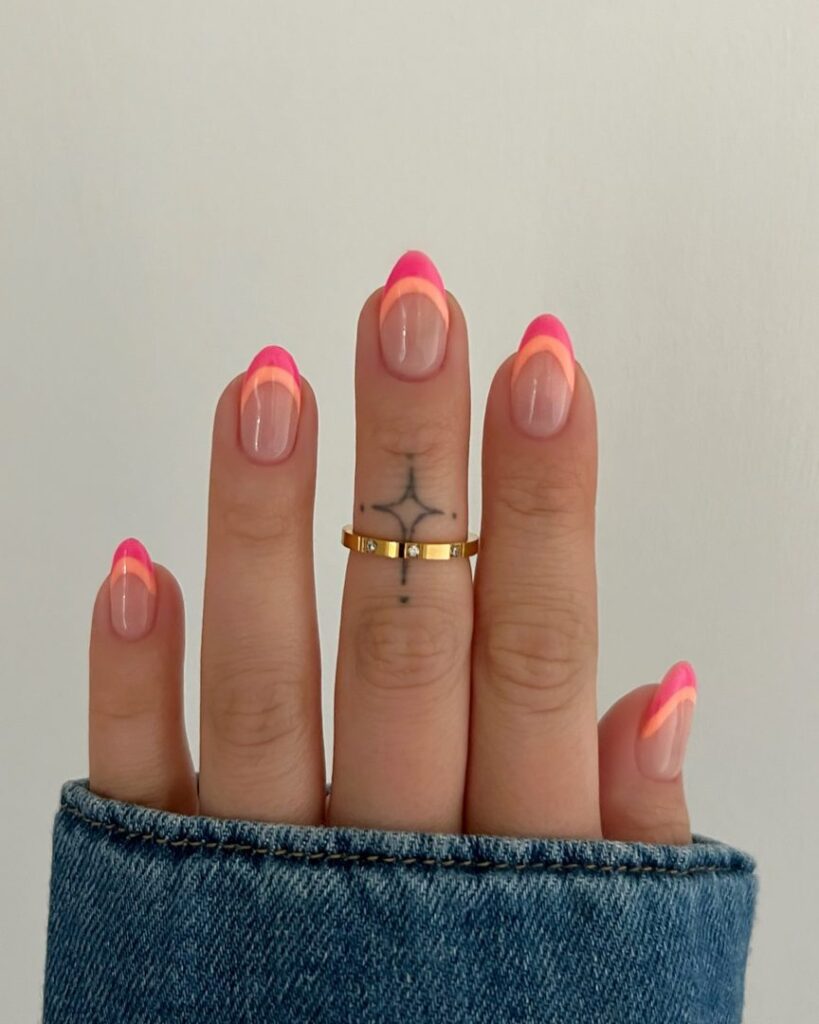 Short round nails with a neon coral-pink outer French tip and a warm orange inner halo tip on a sheer nude base