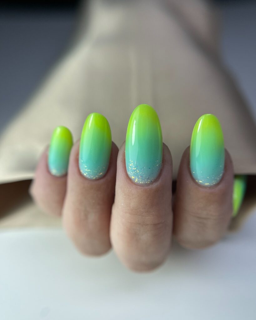 nails with a neon lime green to turquoise ombre gradient and scattered gold flakes at the base