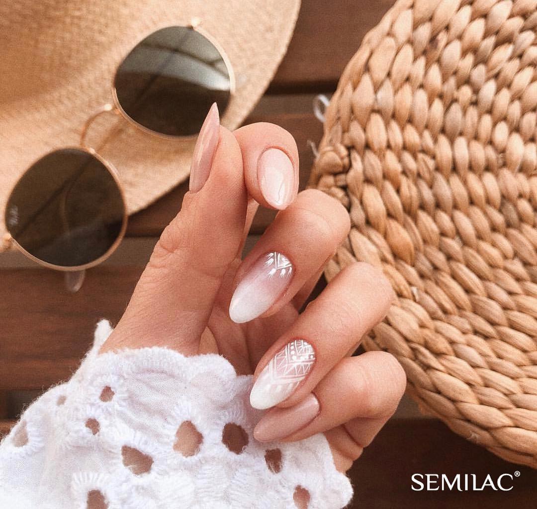 Long almond nails in soft nude with white geometric tribal pattern accent nail, styled with straw hat and sunglasses