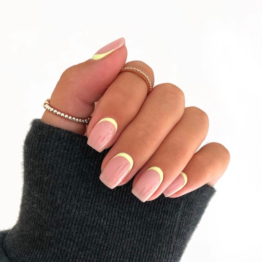 Short square nails with soft pastel yellow French tips on a sheer pink base