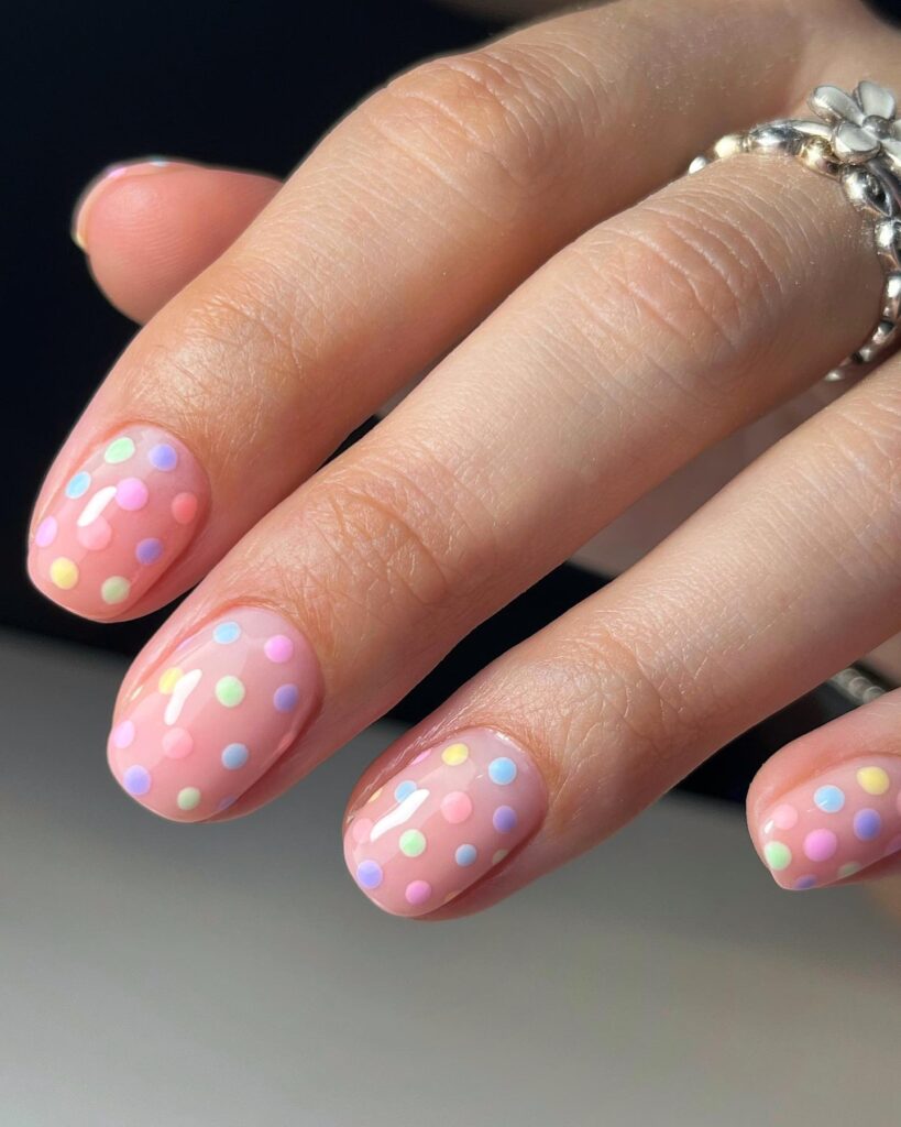 Short round pink nails scattered with pastel confetti dots in mint, lilac, yellow, and peach