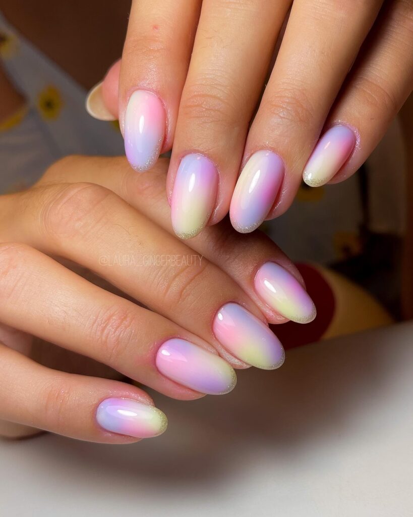 Short almond nails with a soft pastel pink, lavender, and yellow aurora ombre with gold glitter base