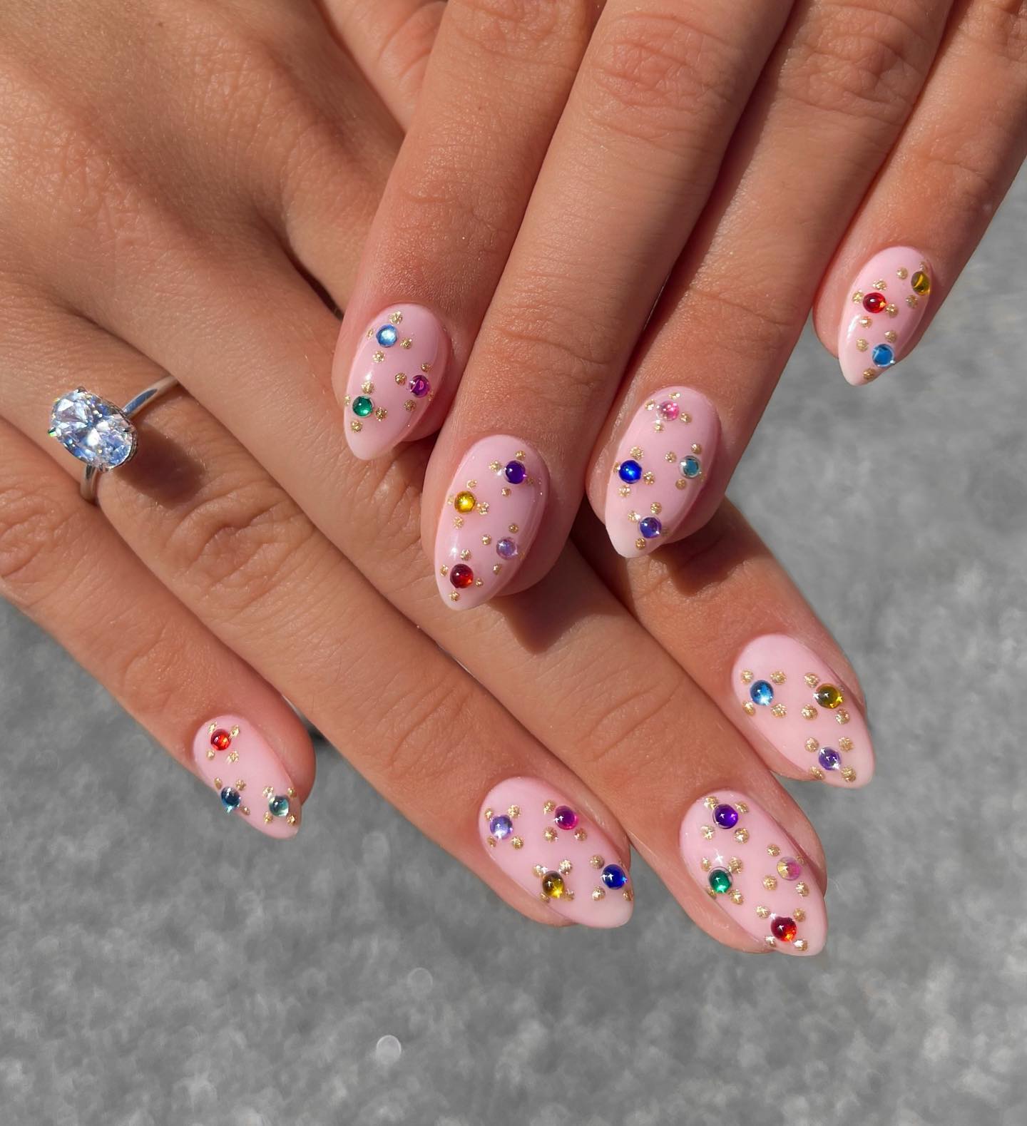 Pale pink almond nails with a scattered array of multicolour rhinestones in various sizes