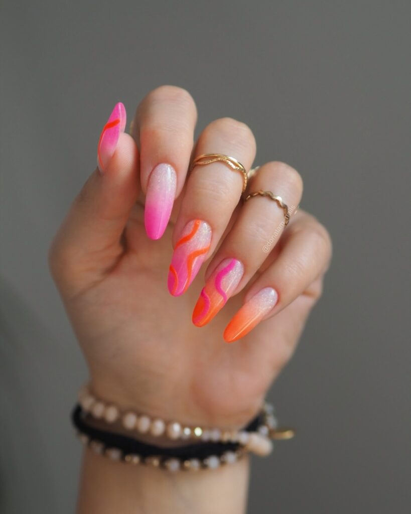 Long square nails with a peach to orange ombre gradient and scattered gold foil at the base