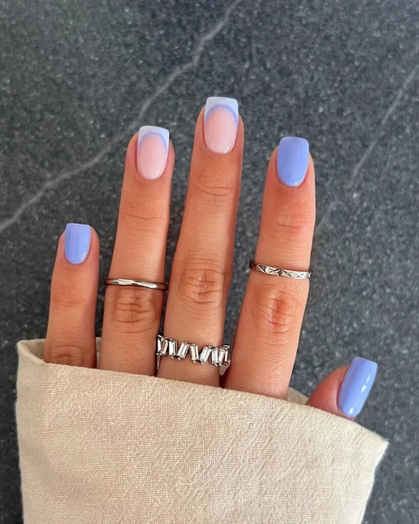Short square nails with periwinkle blue solid colour and a white French tip accent nail on soft pink base