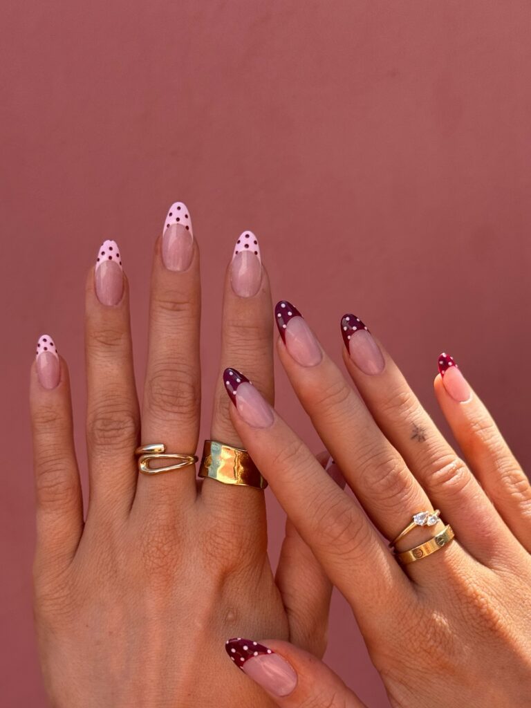 Almond French tip nails in blush pink on one hand and deep plum on the other, both adorned with white polka dots