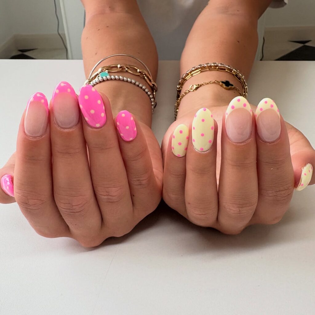 Oval nails featuring hot pink French tips with yellow polka dots on one hand, and butter yellow French tips with pink polka dots on the other