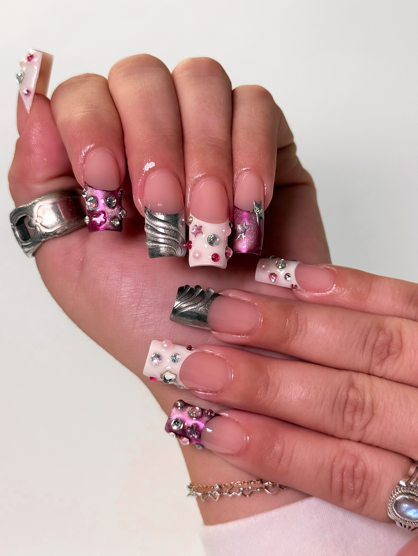 Square French tip nails in pink with silver chrome accents, metallic tips, and scattered rhinestones