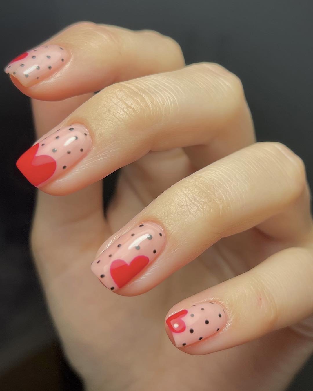 Sheer pink short square nails scattered with tiny black polka dots and red heart accents