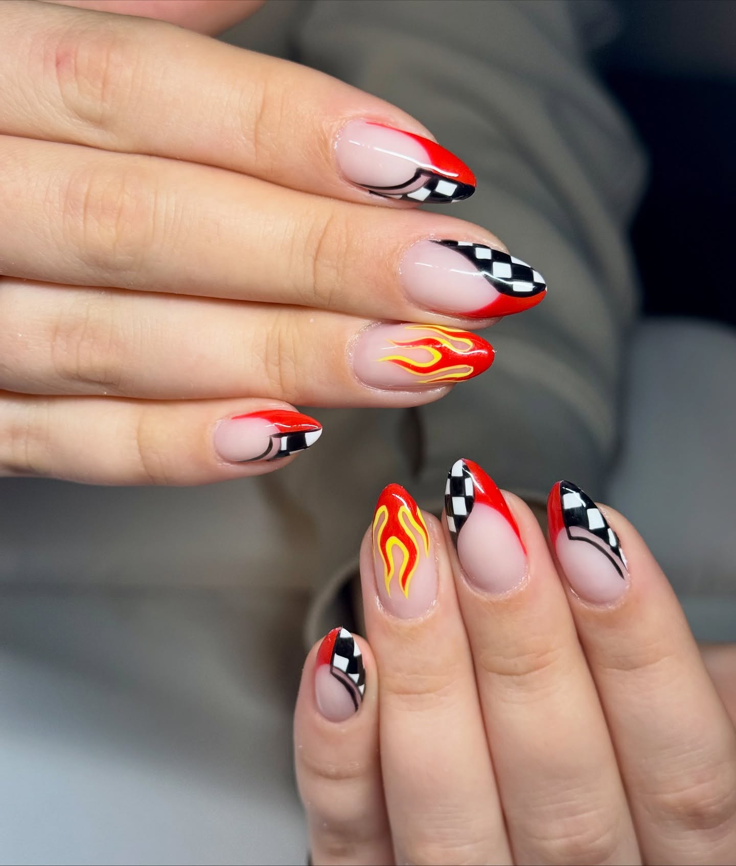 Almond nails with alternating red and yellow flame tips and black-and-white racing checkered tips on a nude base